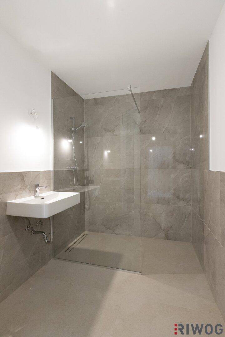 Modernes Badezimmer mit ebenerdiger Dusche und eleganten grauen Fliesen an Wänden und Boden.
