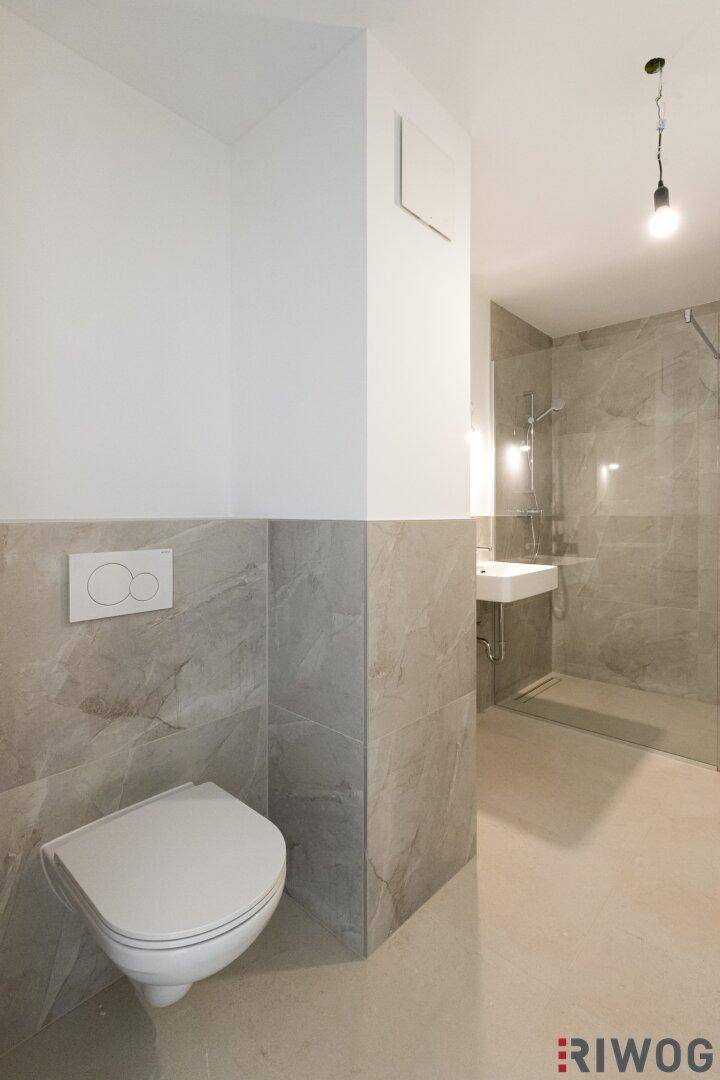 Funktionales Badezimmer mit wandhängendem WC, Dusche und modernem Waschbecken.