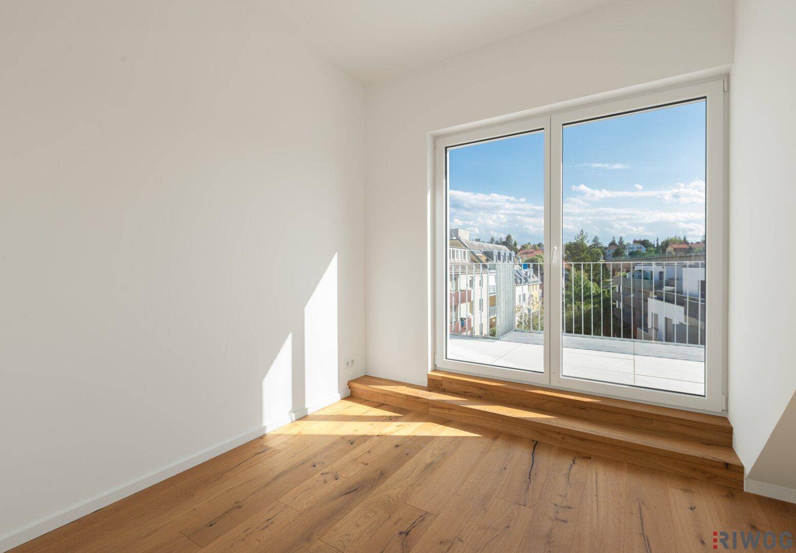 Helles Zimmer mit Holzboden und Zugang zu einem Balkon, ideal als Schlaf- oder Arbeitszimmer.