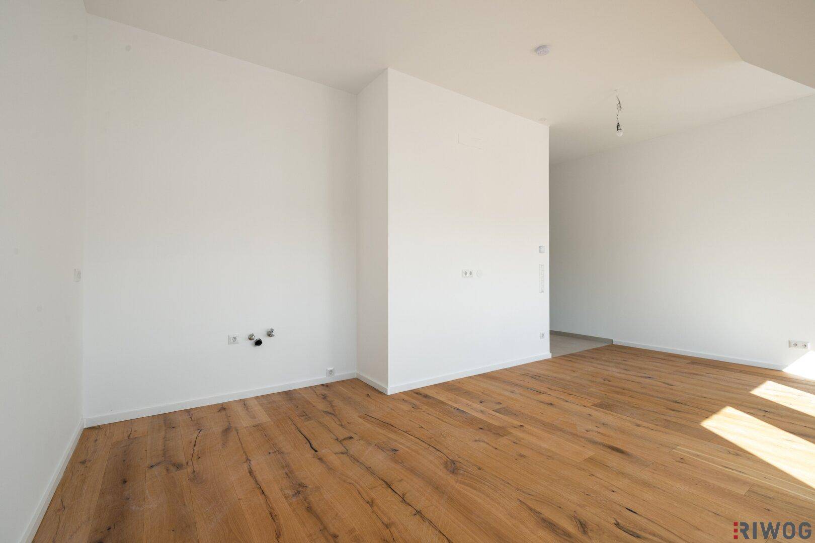 Leerer Raum mit Holzboden und Anschlüssen an der Wand, bereit für die individuelle Gestaltung.