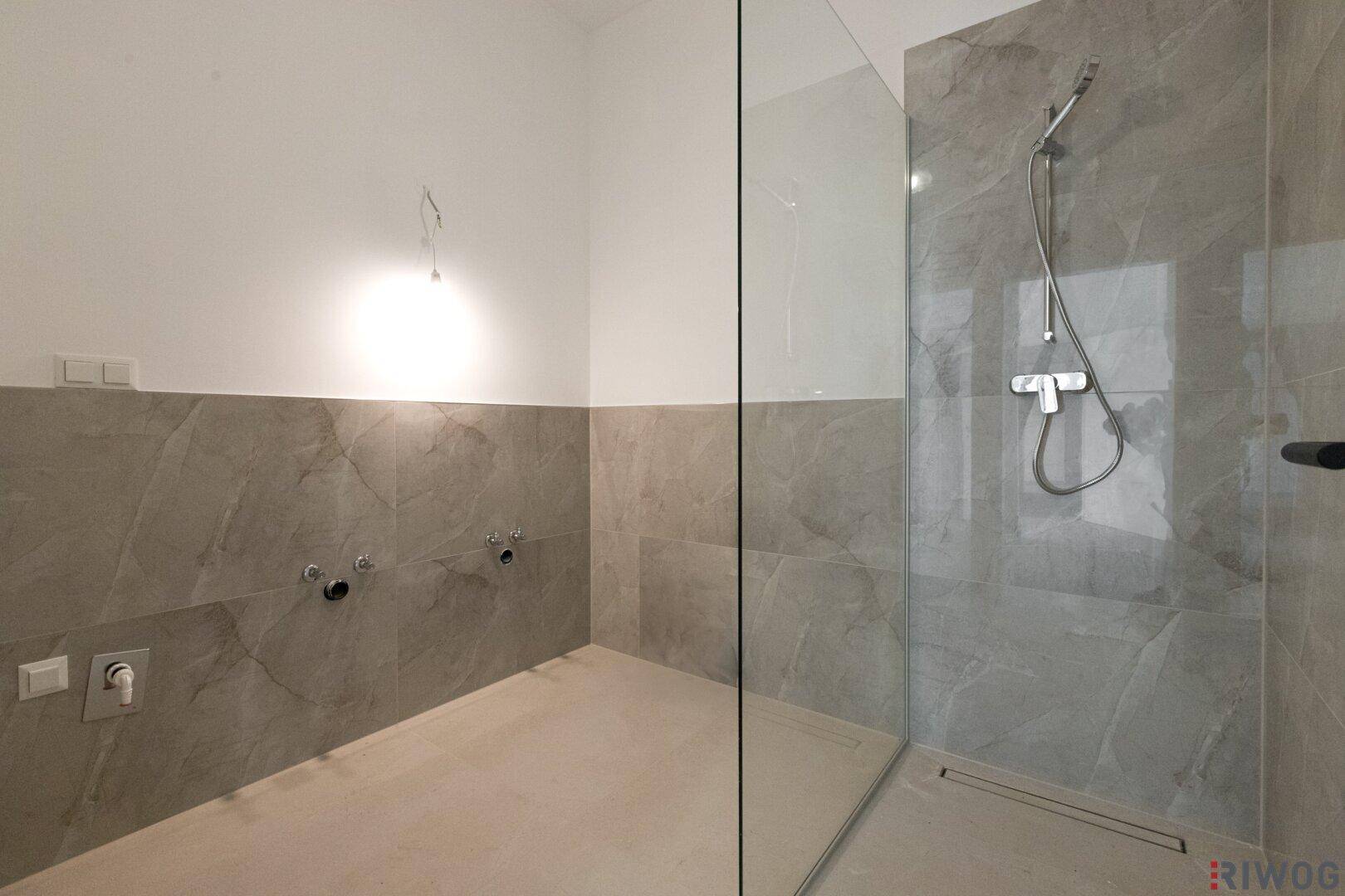 Modernes Badezimmer im Bau mit großformatigen grauen Fliesen und begehbarer Dusche.
