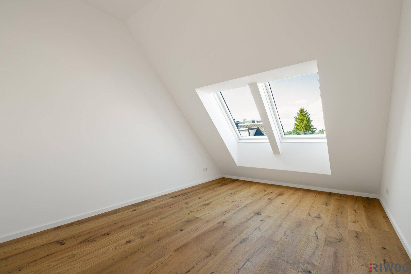 Helles Schlafzimmer im Dachgeschoss mit Holzboden und schrägen Wänden, durch Dachfenster belichtet.