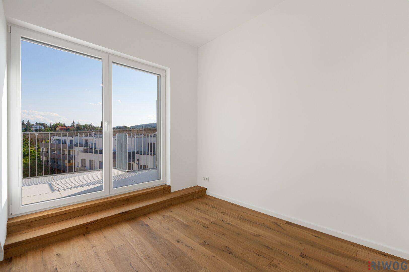 Heller Raum mit Holzboden und großer Terrassentür, die viel Tageslicht hereinlässt.