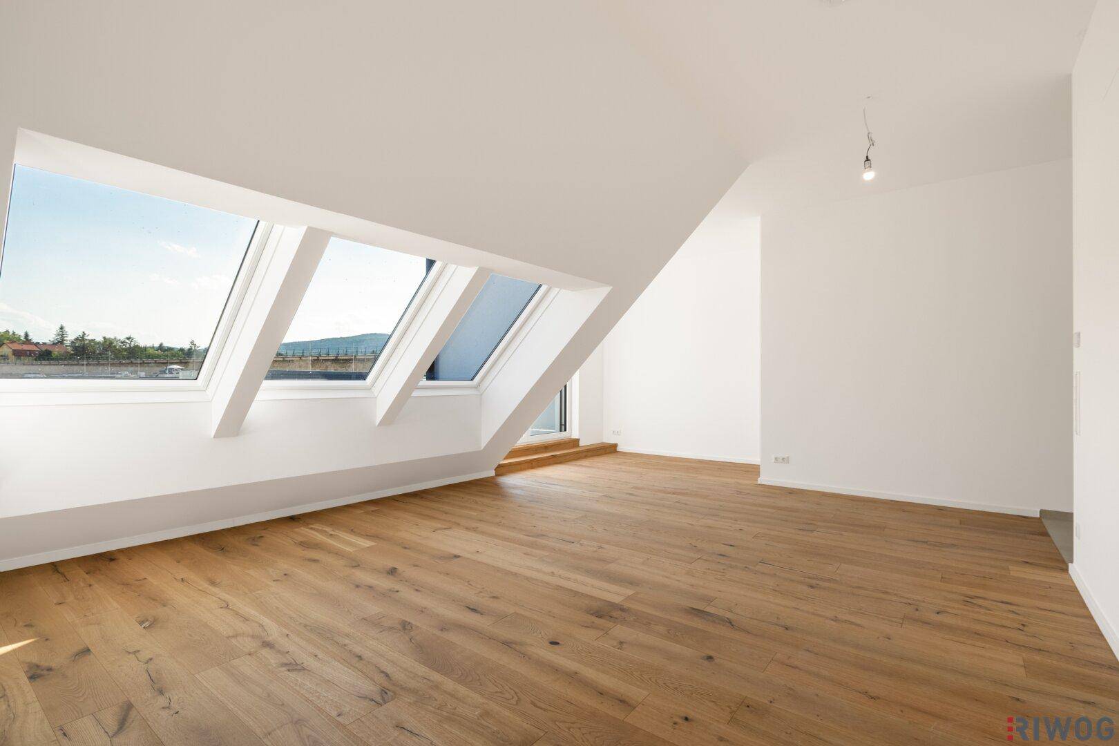 Lichtdurchfluteter Dachgeschossraum mit Holzboden, großen Dachfenstern und weitem Ausblick.