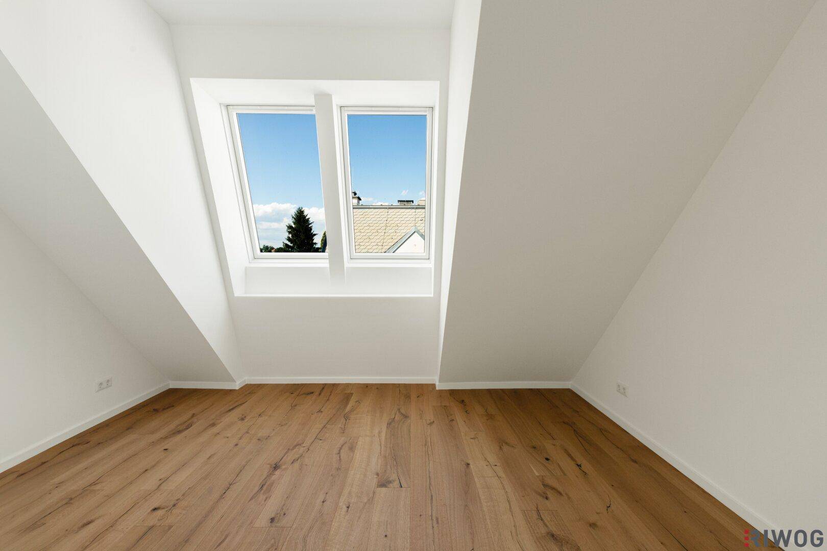 Dachgeschossraum mit Holzboden und zwei großen Dachfenstern, die den Raum erhellen.