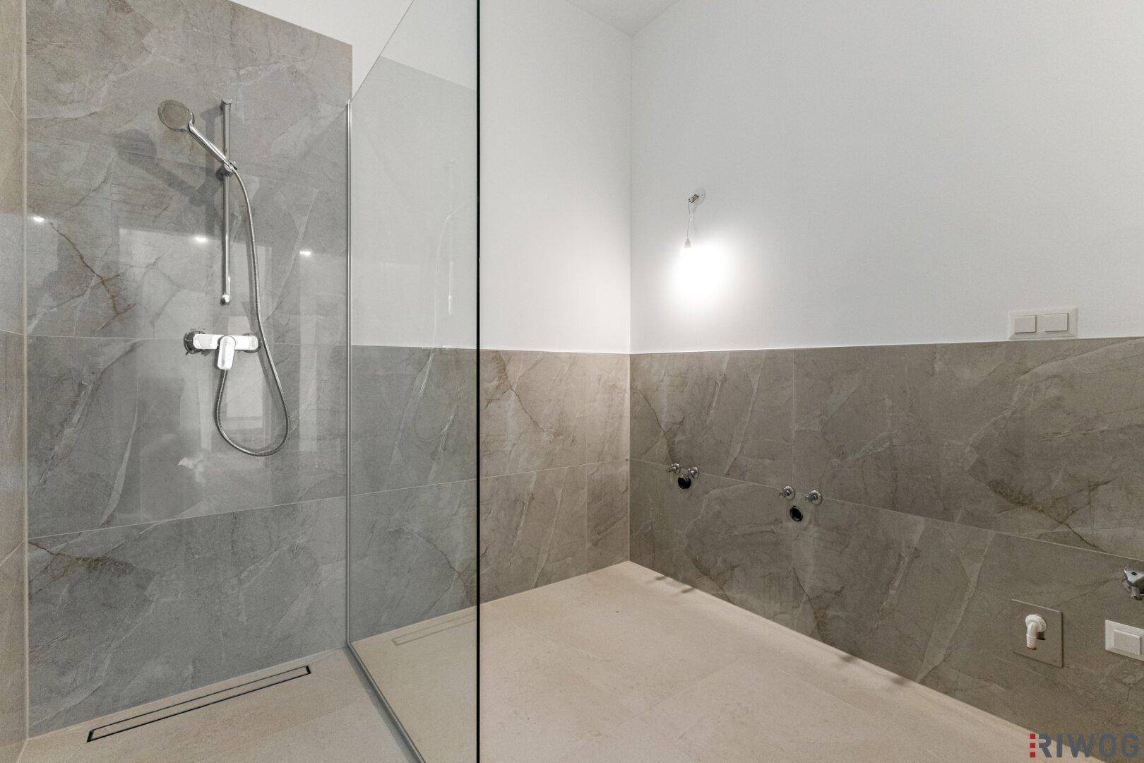 Modernes Badezimmer mit begehbarer Dusche und eleganten grauen Fliesen an Wänden und Boden.