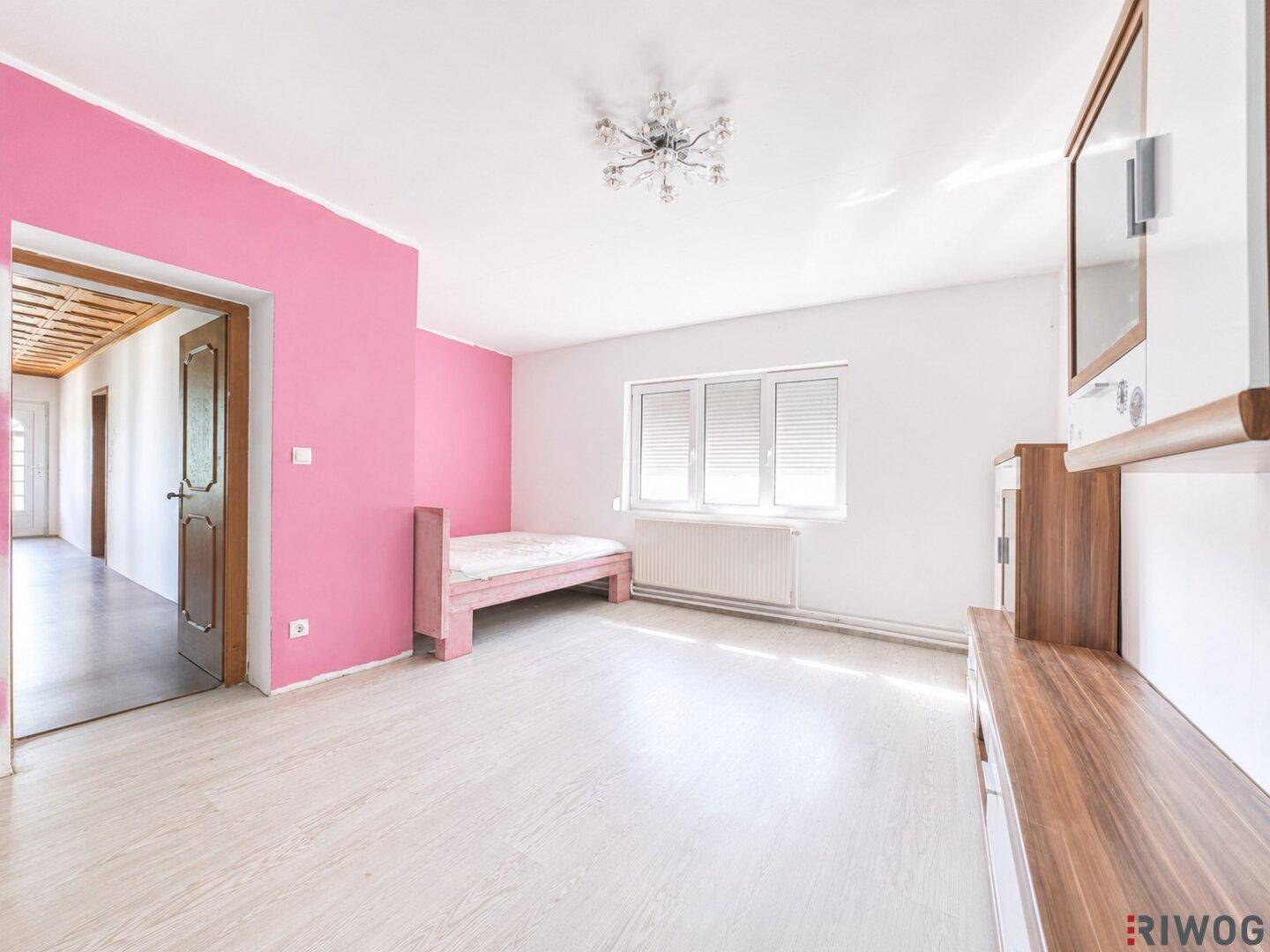 Schlafzimmer mit pinker Akzentwand, hellem Laminatboden und Fenster.