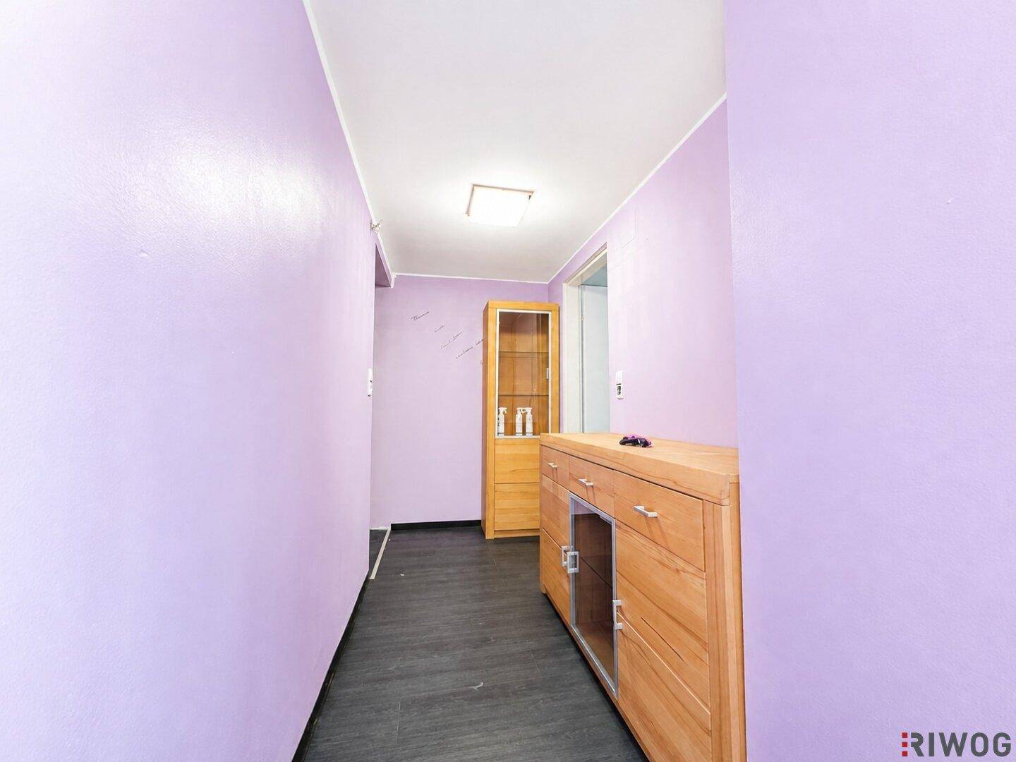Schmaler Flur mit lila Wänden, dunklem Laminatboden und Holzschrank.