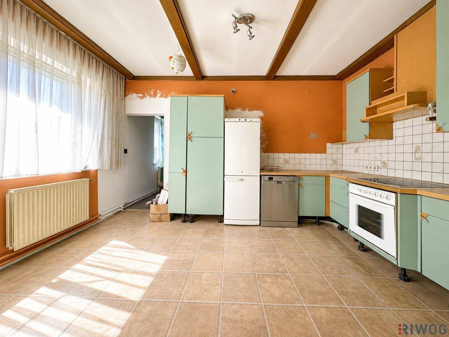 Geräumige Küche mit orangefarbenen Wänden, hellgrünen Schränken und Fliesenboden.