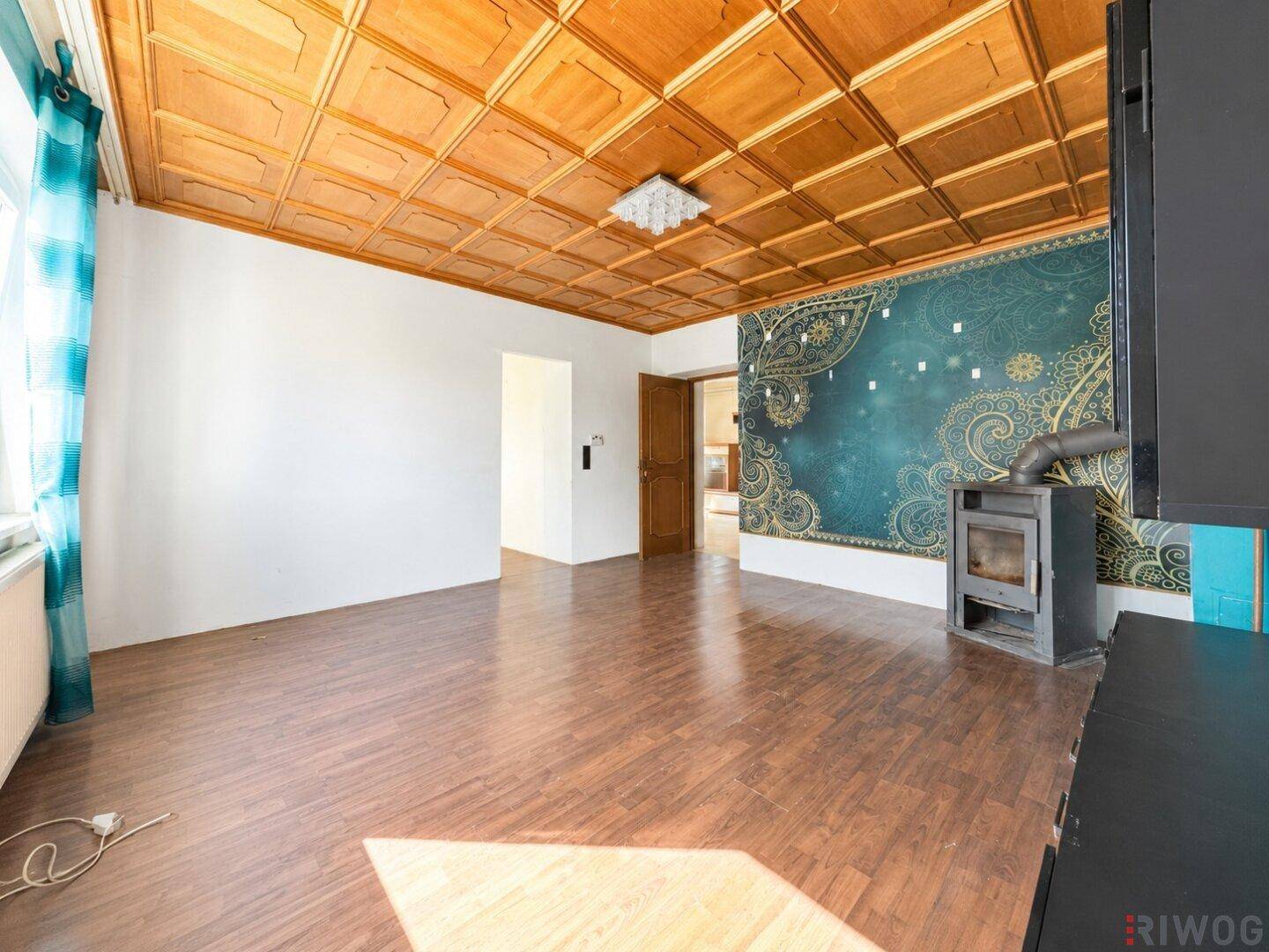 Wohnzimmer mit Holzkassettendecke, Kaminofen und dunklem Laminatboden.