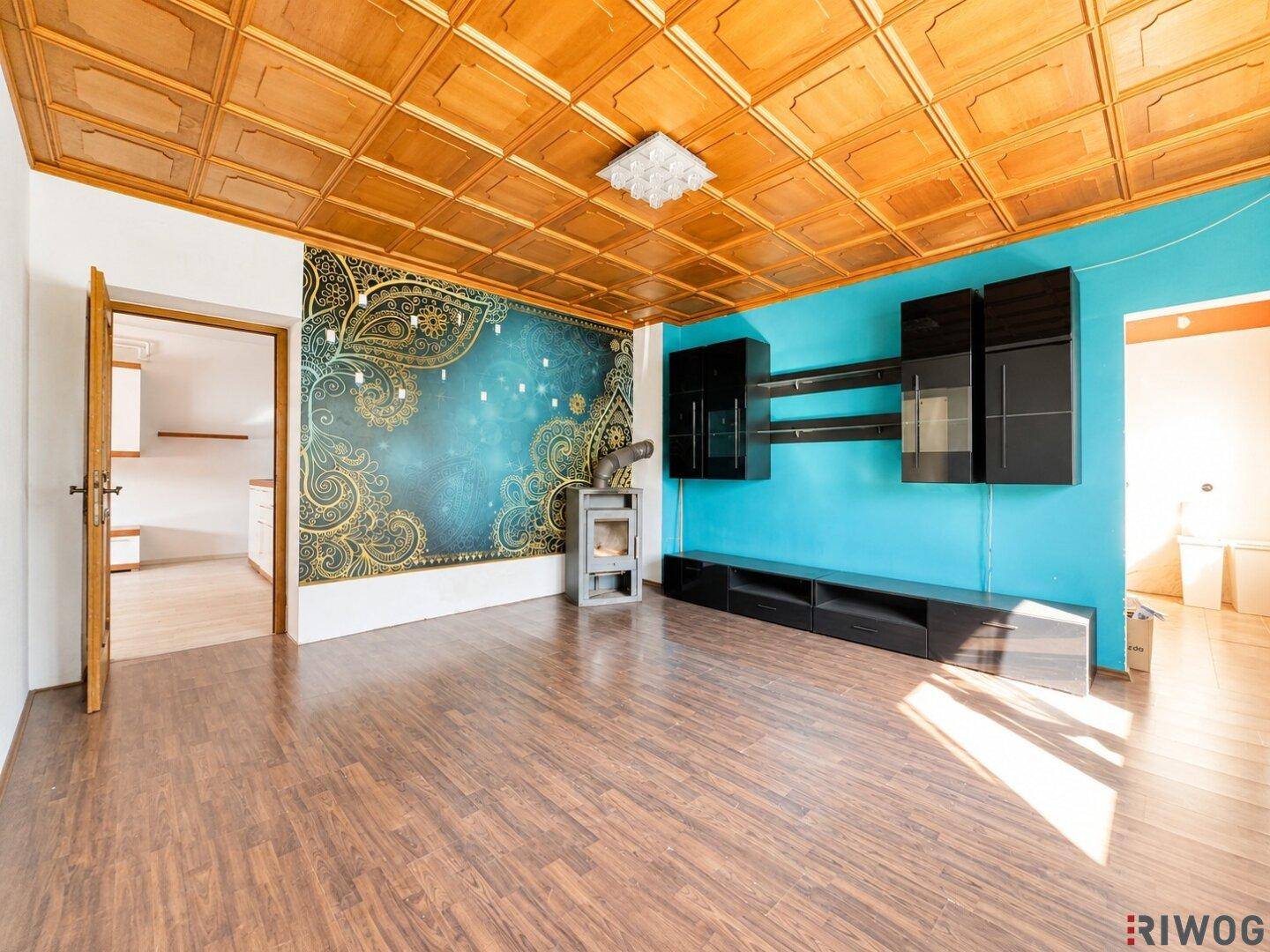 Wohnzimmer mit Holzkassettendecke, Kaminofen und Blick in die Küche.