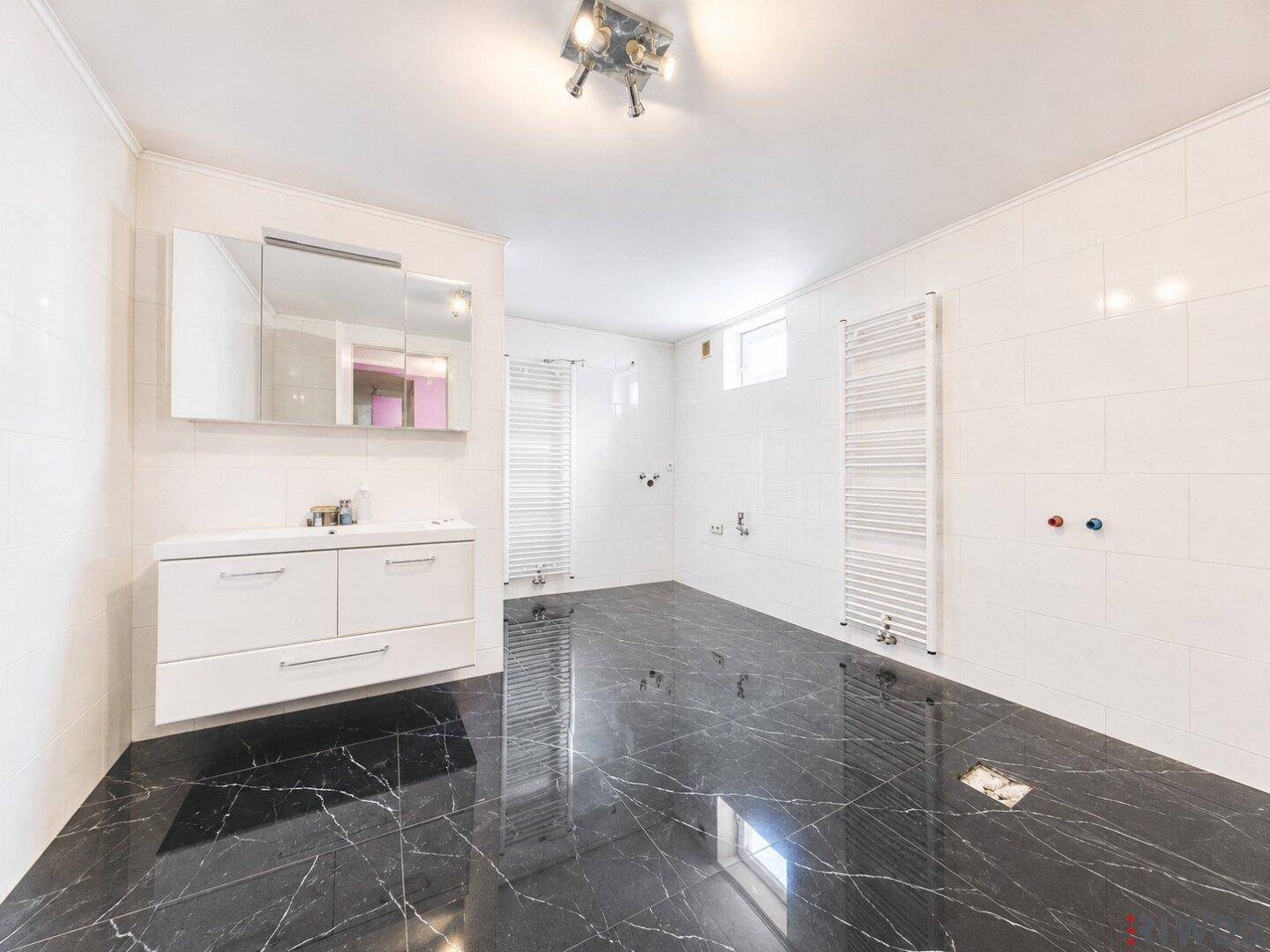Modernes Badezimmer mit schwarzen Marmorfliesen, weißem Waschtisch und Spiegelschrank.