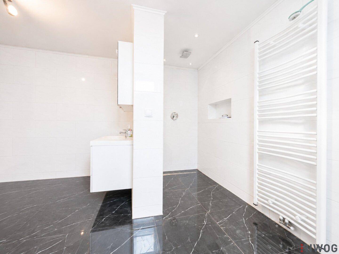 Modernes Badezimmer mit schwarzen Marmorfliesen, weißem Waschtisch und Duschbereich.