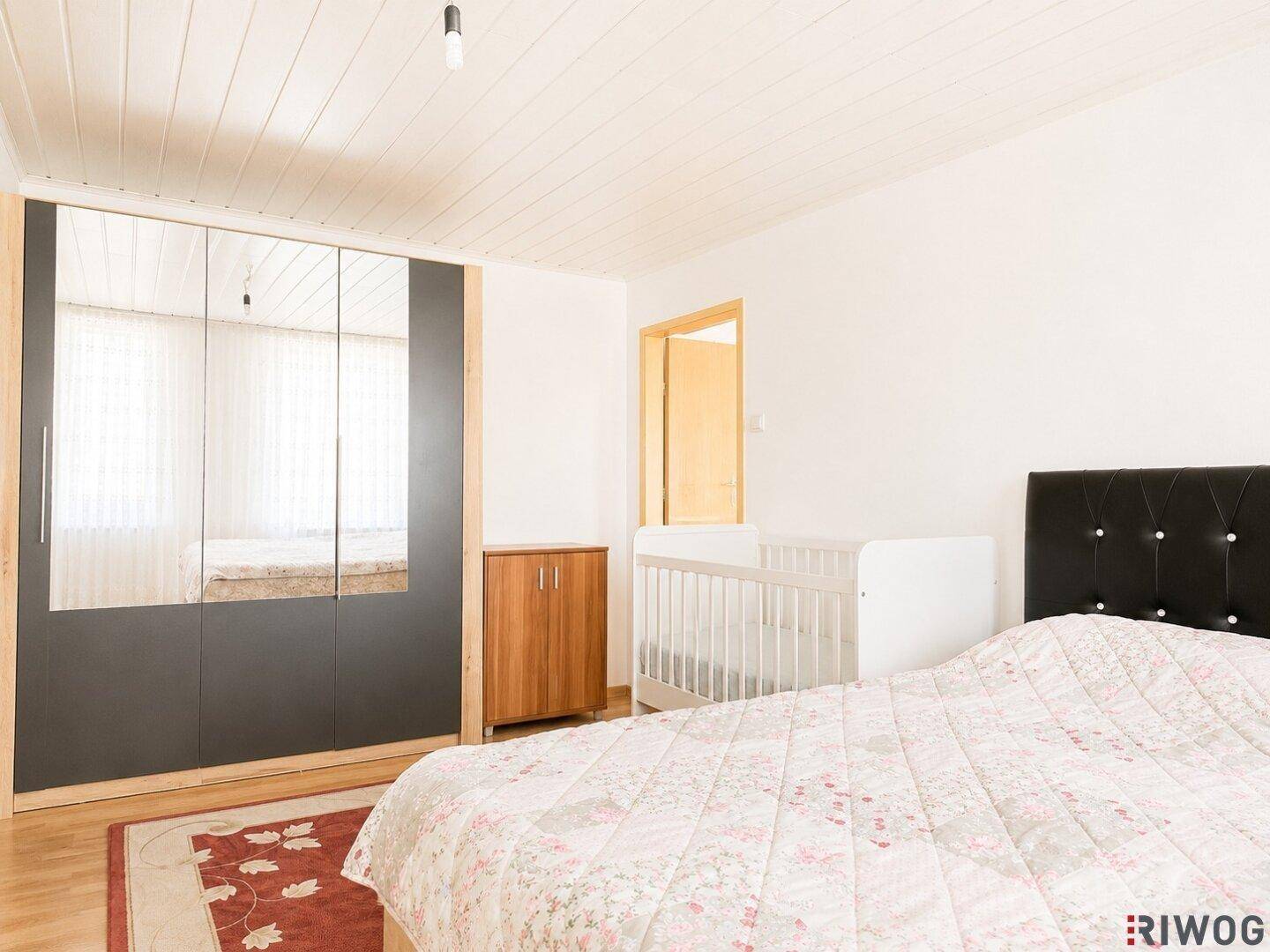 Helles Schlafzimmer mit großem Kleiderschrank, Doppelbett und Babybett, ideal für Familien.