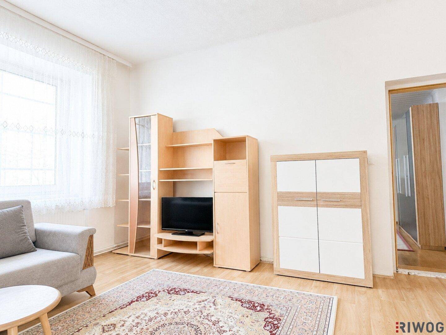Gemütliches Wohnzimmer mit hellem Holzboden, Sofa und TV-Möbeln, durchflutet von Tageslicht.