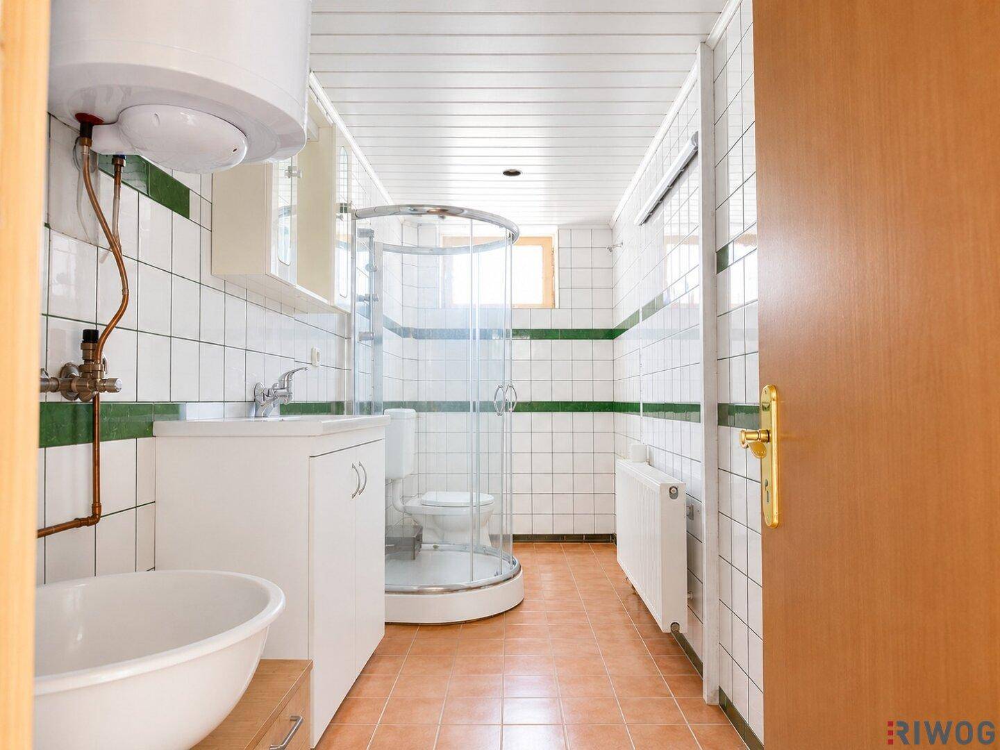 Badezimmer mit Duschkabine, Waschbecken und WC, ausgestattet mit grünen Akzentfliesen.
