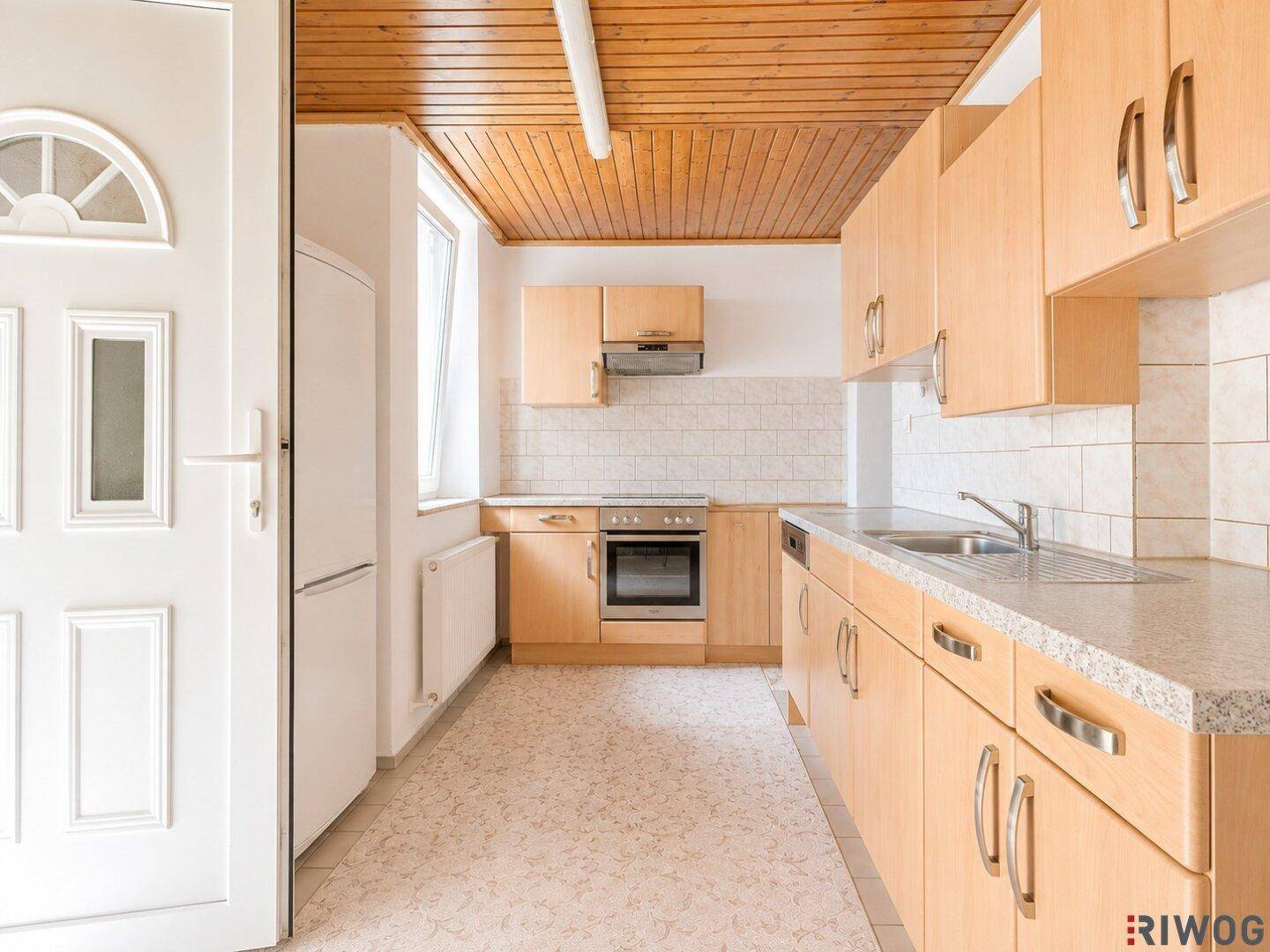 Helle Küche mit Holzschränken, integrierten Geräten und Fenster, das viel Licht hereinlässt.