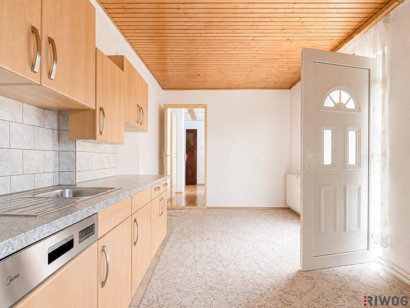 Geräumige Küche mit Holzschränken, Spülmaschine und Zugang zu einem weiteren Raum.