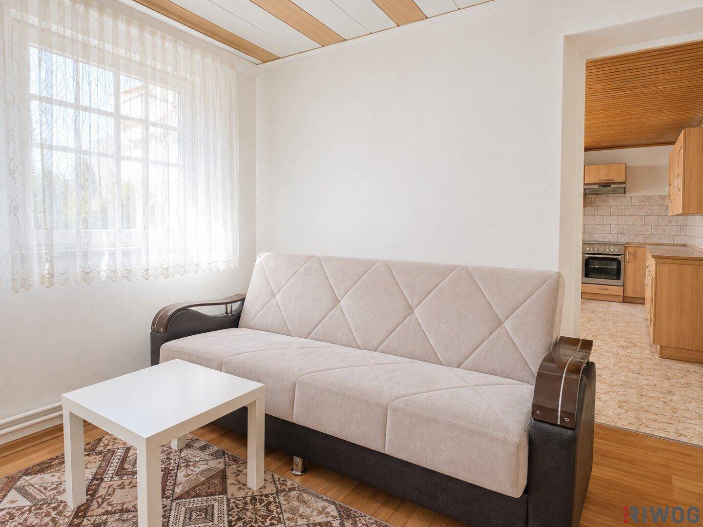 Gemütlicher Wohnbereich mit beigem Sofa, kleinem Couchtisch und Fenster mit Vorhängen.
