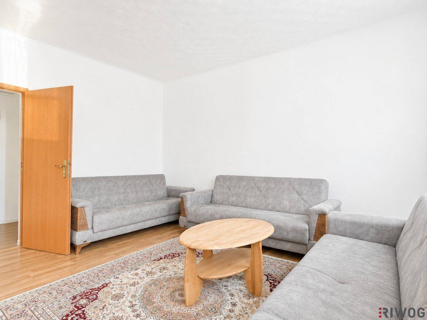 Großzügiges Wohnzimmer mit mehreren grauen Sofas und einem ovalen Holztisch auf einem Teppich.