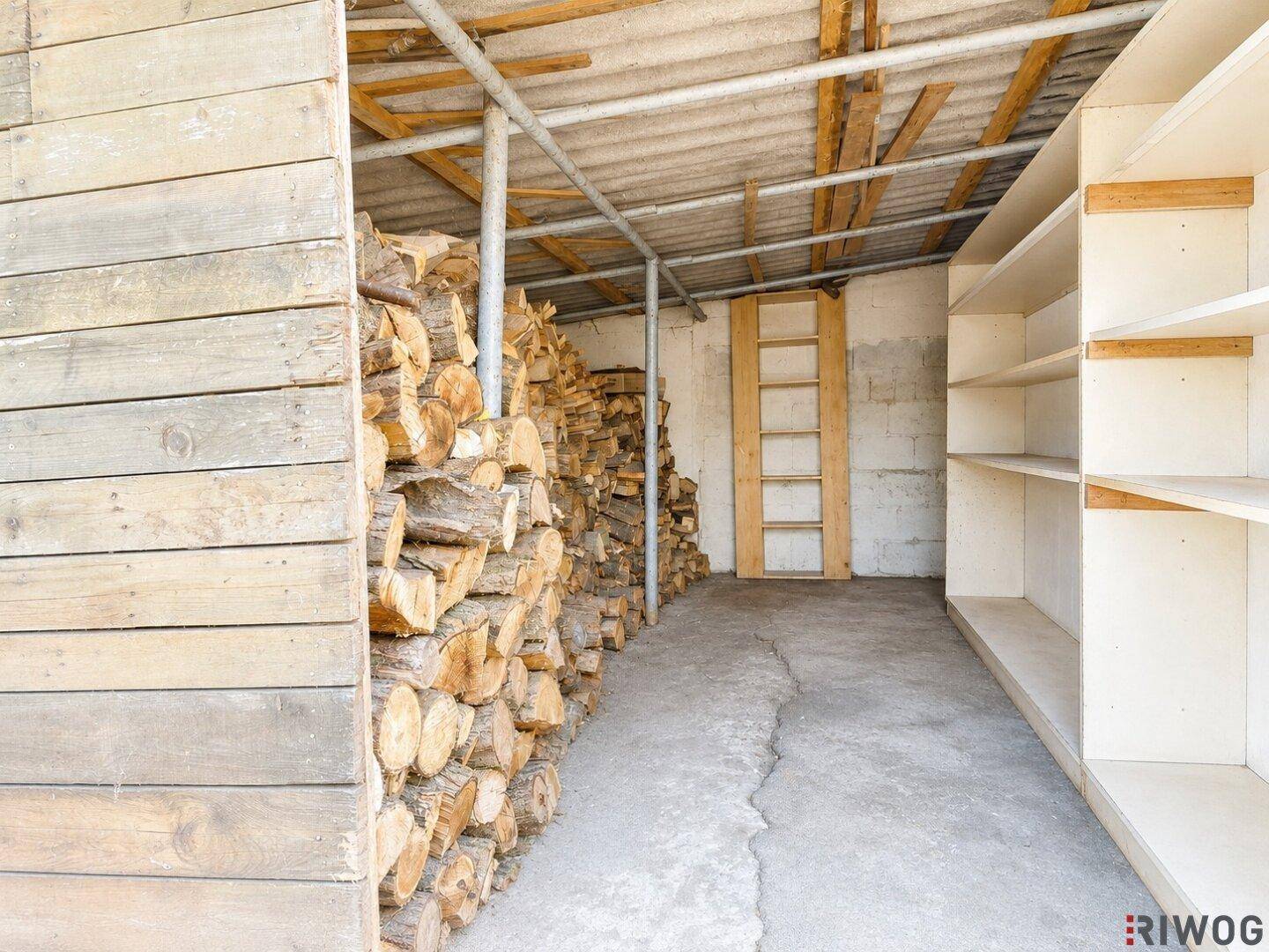 Überdachter Lagerbereich mit gestapeltem Brennholz und Regalen, ideal für Gartenutensilien.
