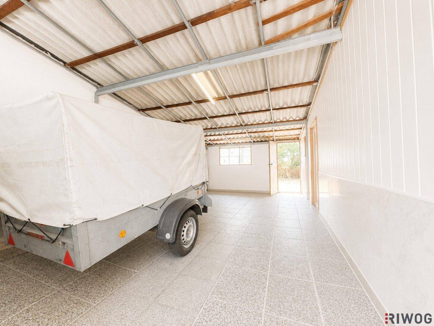 Geräumige Garage mit Betonboden und einem Anhänger, bietet viel Platz für Fahrzeuge.