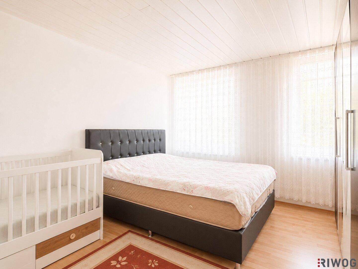 Helles Schlafzimmer mit Doppelbett und Babybett, ideal für eine junge Familie.
