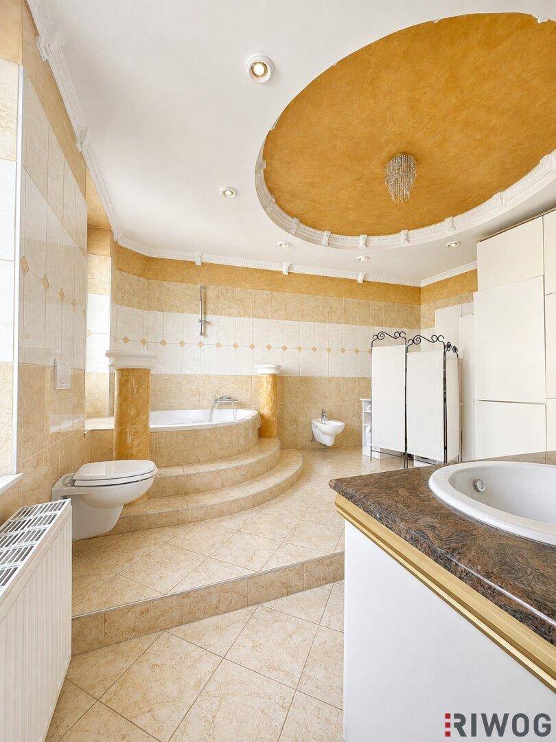 Großes Badezimmer mit beigefarbenen Fliesen, erhöhter Badewanne und Doppelwaschbecken.