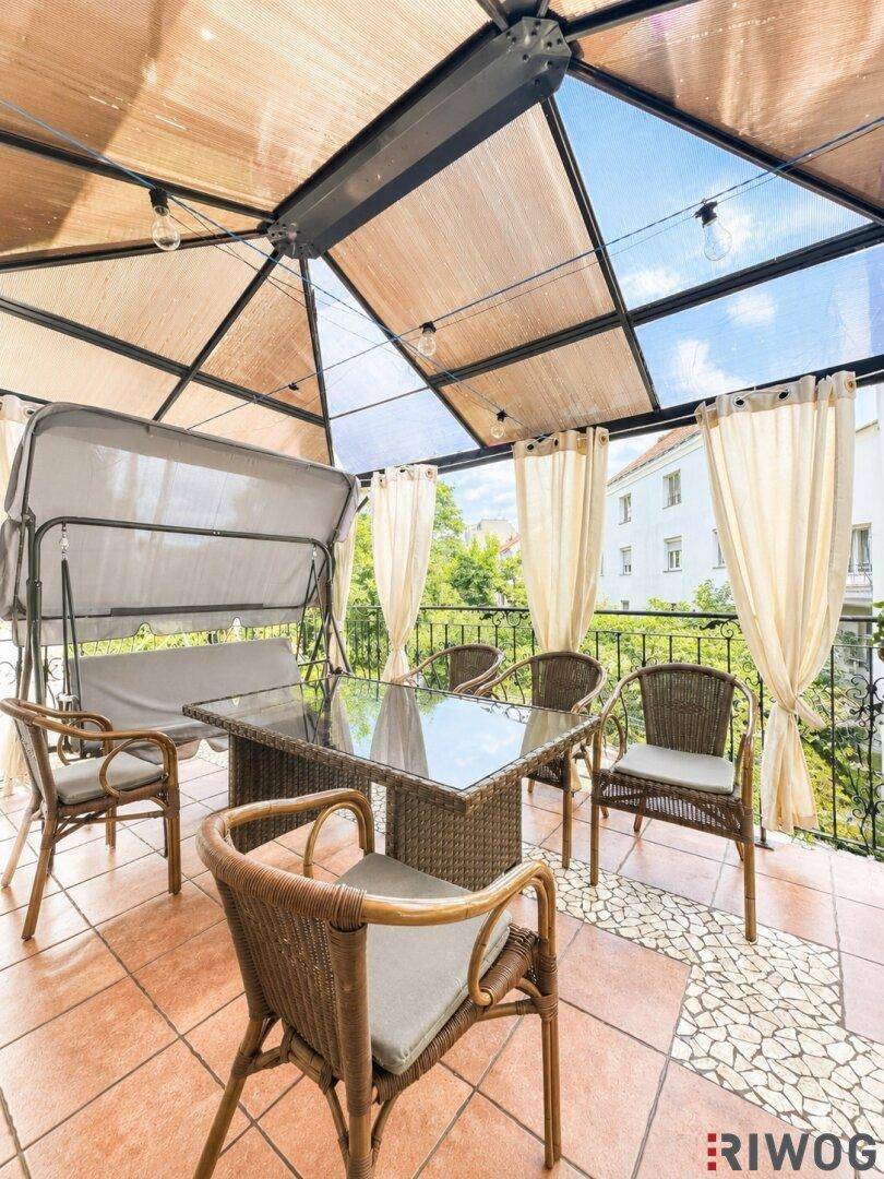 Überdachte Terrasse mit Rattanmöbeln, Esstisch und Blick auf die Umgebung.