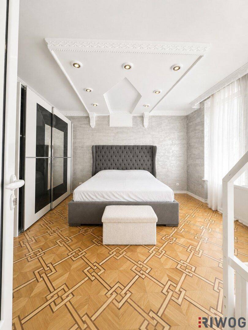 Schlafzimmer mit gemustertem Parkettboden, gepolstertem Bett und integrierten Kleiderschränken.