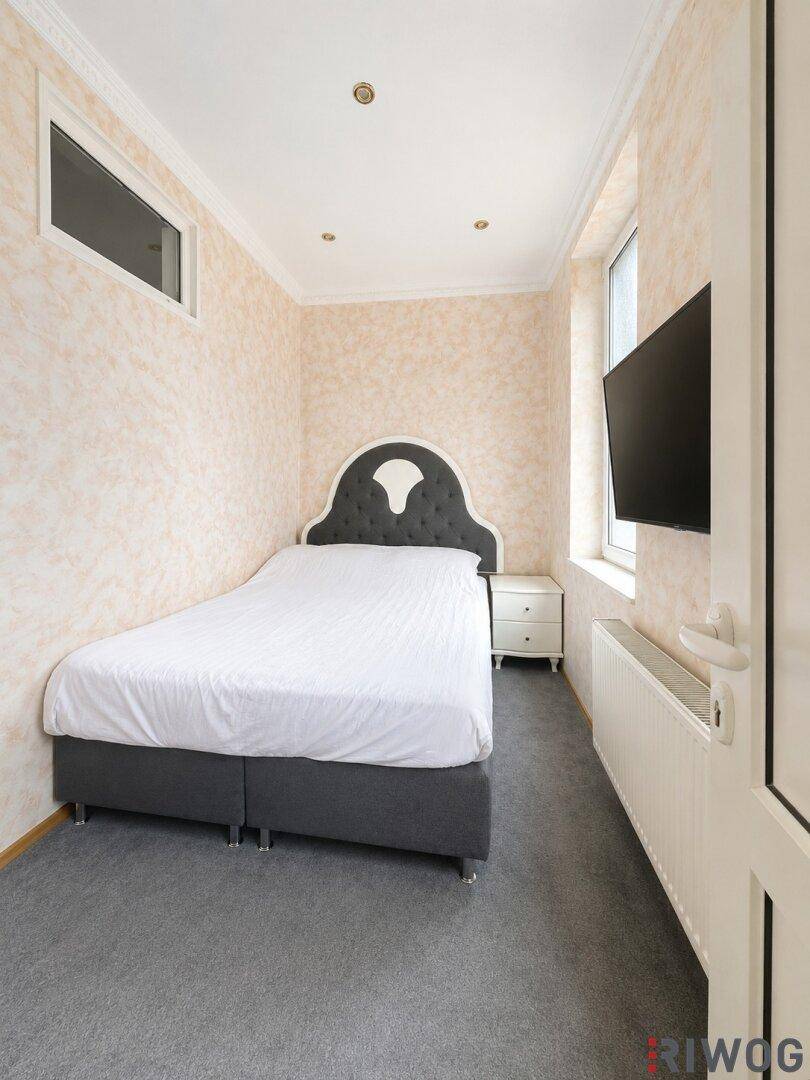 Gemütliches Schlafzimmer mit Teppichboden, Einzelbett und Wandfernseher.