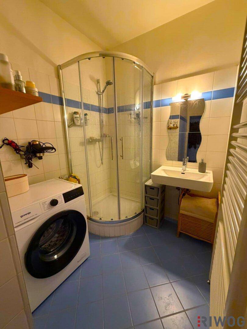 Badezimmer mit blauen Fliesen, Duschkabine, Waschbecken und einer Waschmaschine.