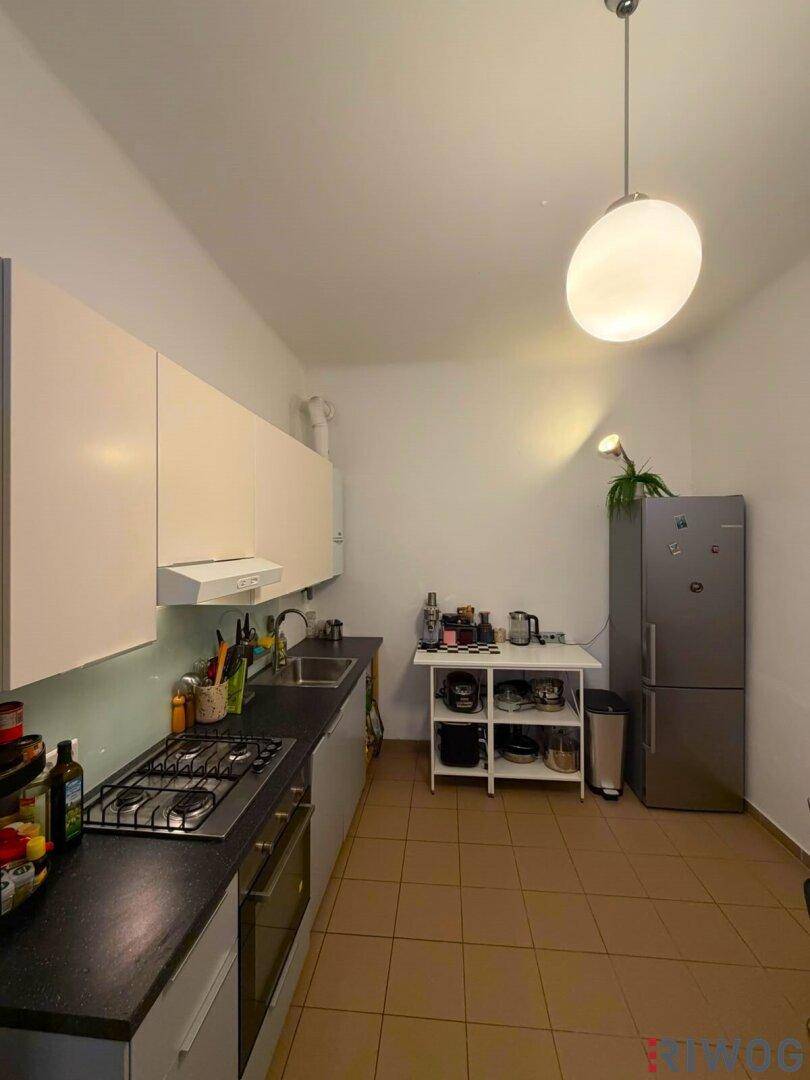 Schmale Küche mit beigen Oberschränken, Gasherd und einem freistehenden Kühlschrank.