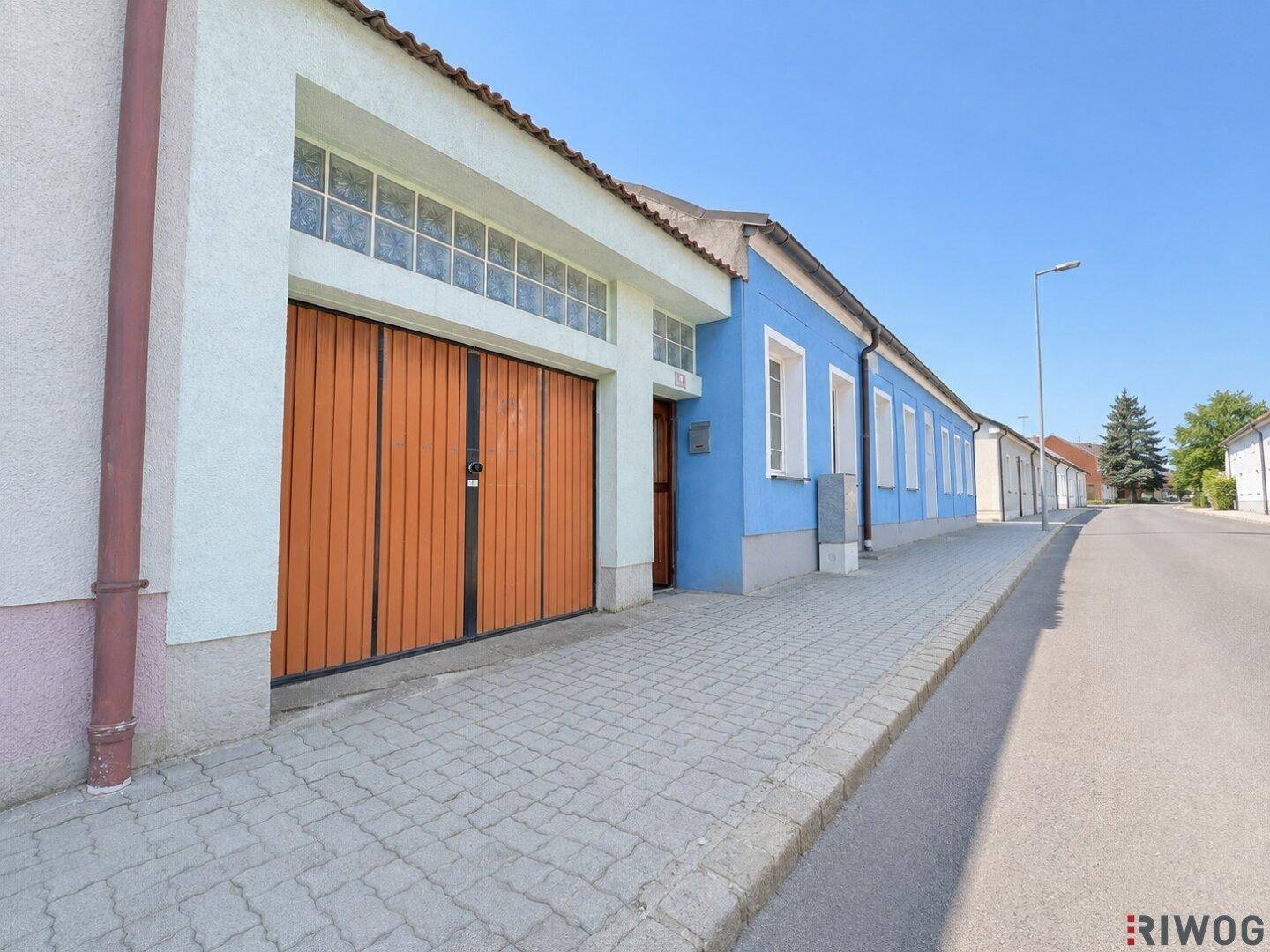 Seitenansicht des blauen Hauses mit angrenzender Garage und gepflastertem Gehweg.