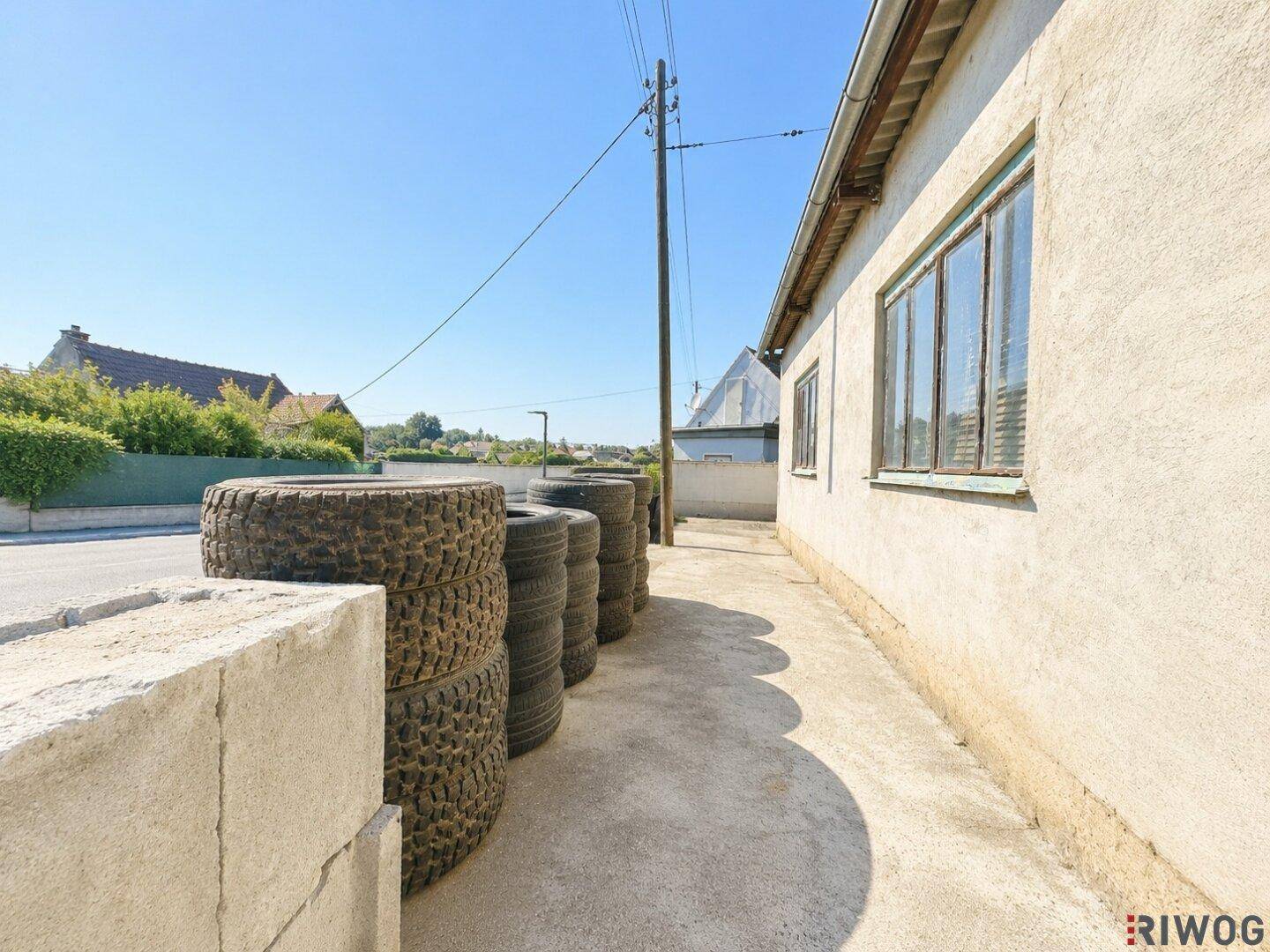 Seitenansicht eines Gebäudes mit Fenstern, einem Betonweg und gestapelten Reifen.