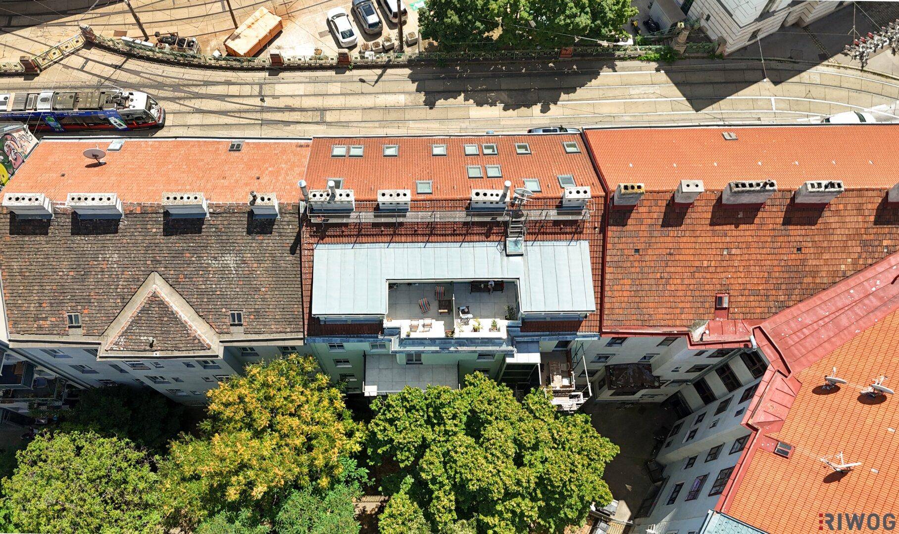 Dachterrasse mit Sitzgelegenheiten auf einem Gebäude, umgeben von anderen Häusern und einer belebten Straße.