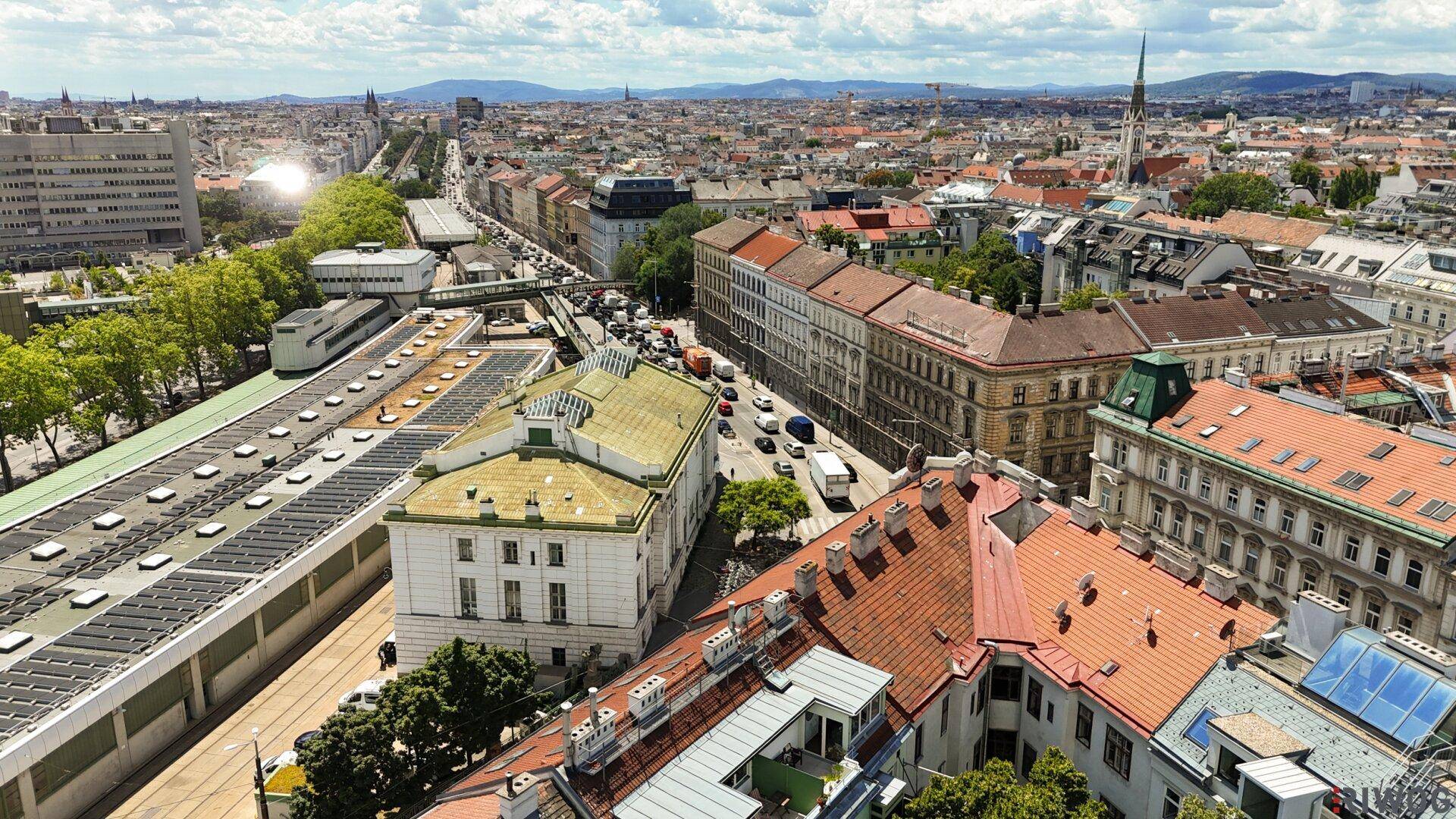 Weitläufige Luftaufnahme einer europäischen Stadt mit zahlreichen Gebäuden, Straßen und Grünflächen unter blauem Himmel.