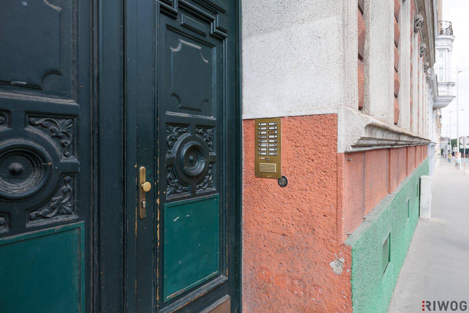 Seitenansicht der verzierten Eingangstür mit Klingelanlage und der farbigen Fassade des Gebäudes.