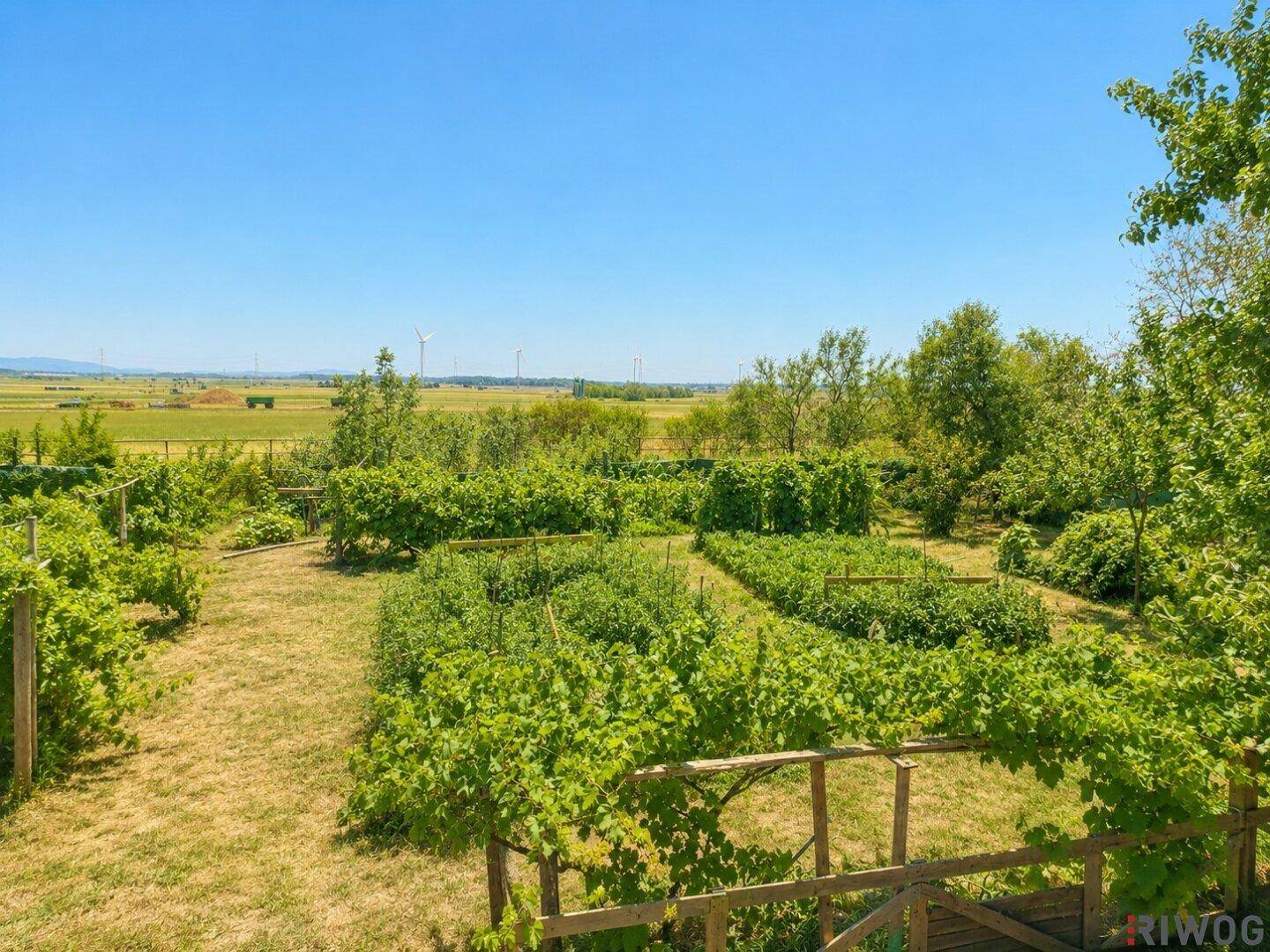 Weitläufiger Garten mit Blick auf die umliegende Landschaft, Felder und Windräder am Horizont.