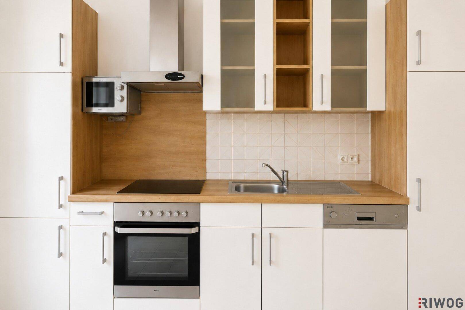 Nahaufnahme der Küchenzeile mit Induktionskochfeld, Backofen, Spüle und integrierter Mikrowelle.