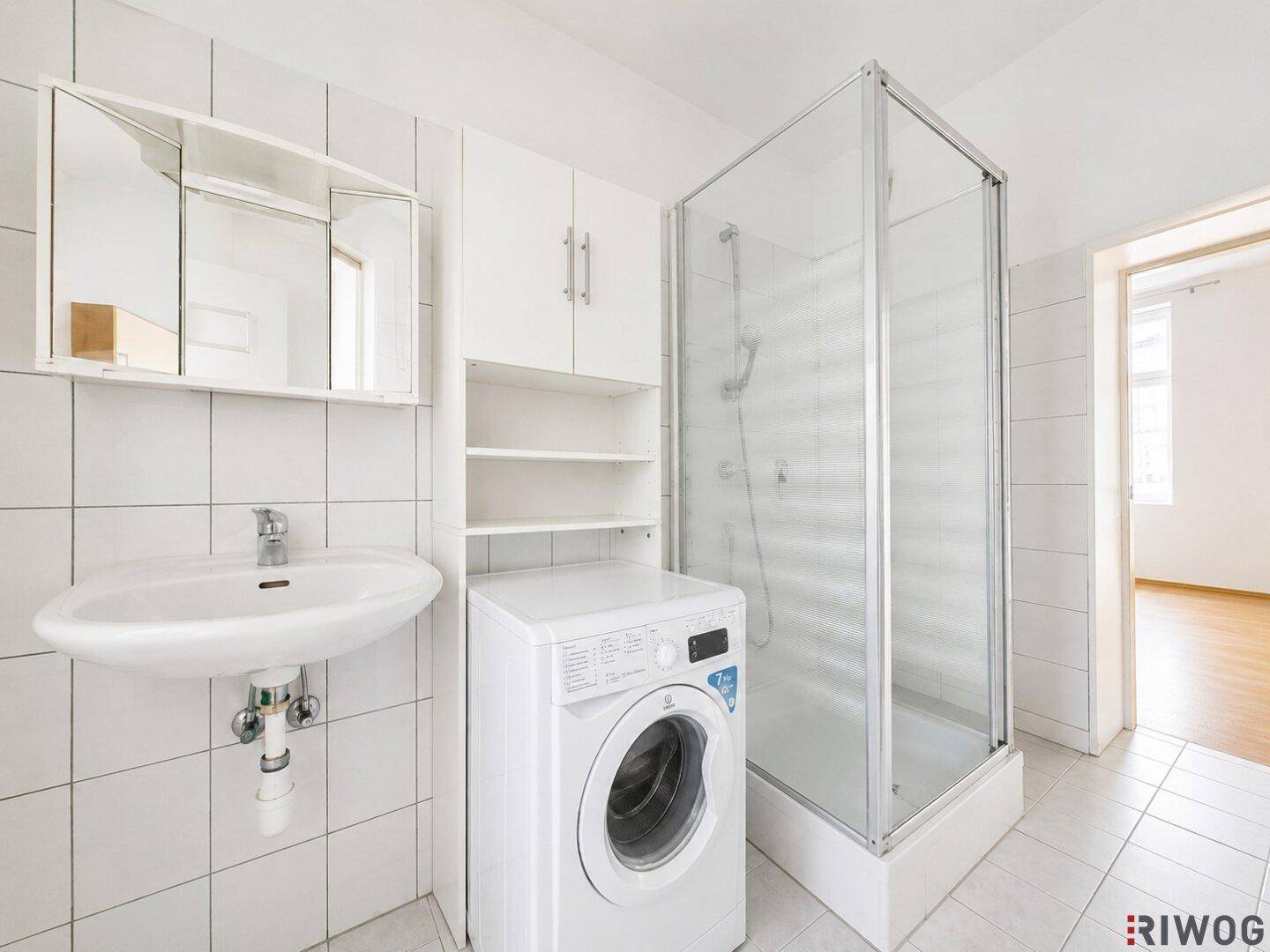 Badezimmer mit Duschkabine, Waschbecken, Spiegelschrank und integrierter Waschmaschine.