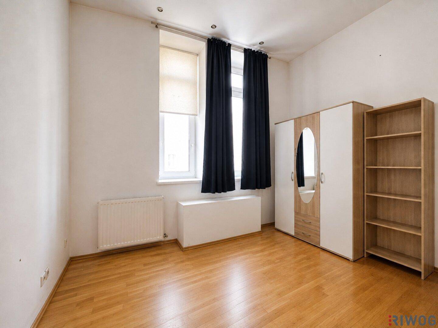 Leeres Zimmer mit Holzboden, Fenster und einem Kleiderschrank mit Spiegeltür.