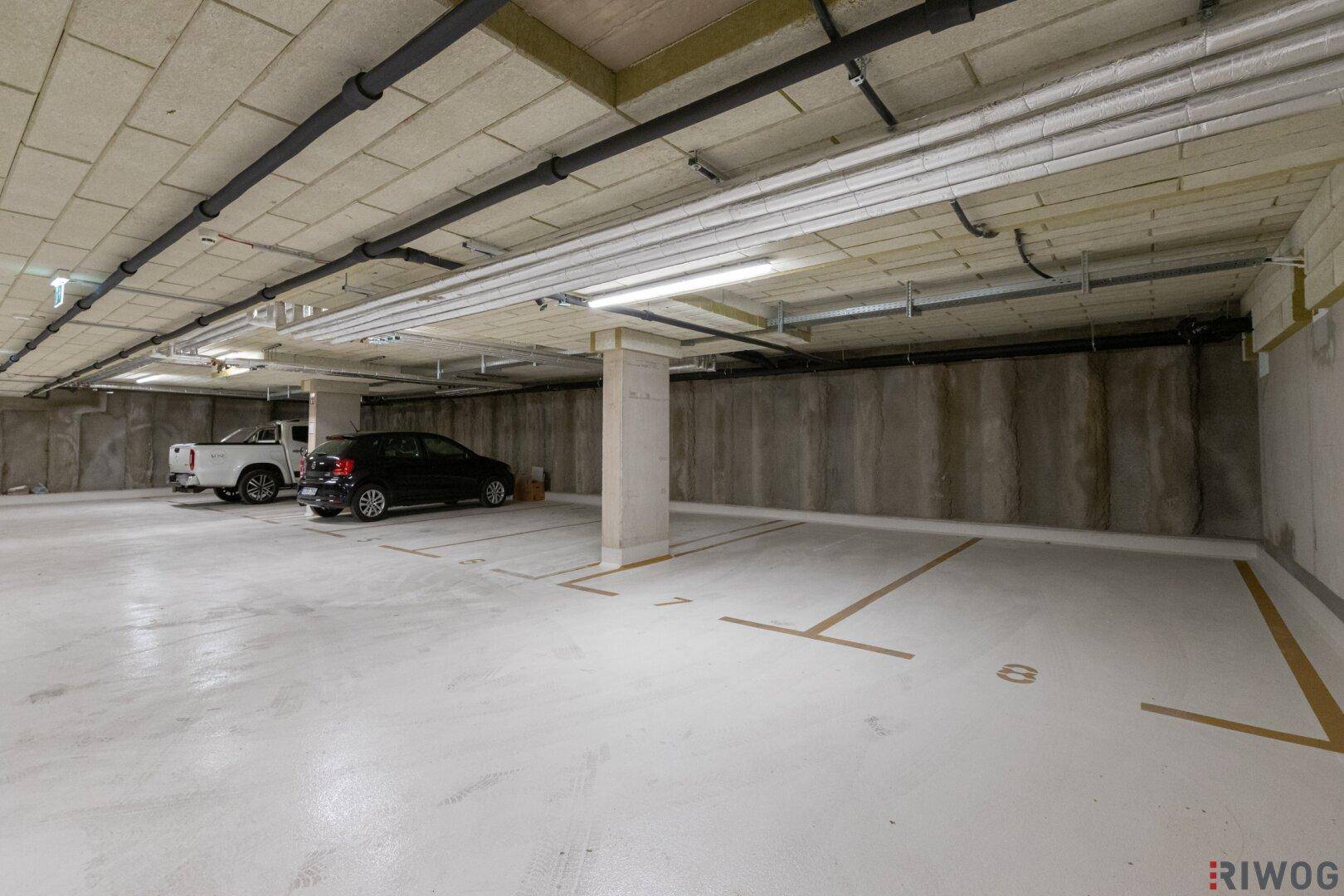 Geräumige Tiefgarage mit markierten Stellplätzen und geparkten Fahrzeugen unter dem Gebäude.