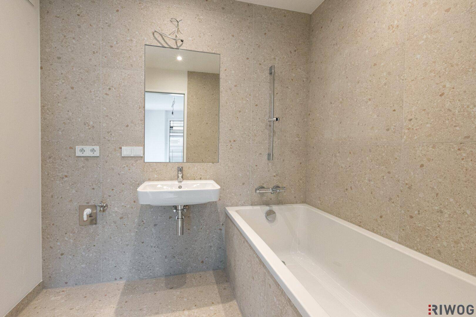 Modernes Badezimmer mit Badewanne, Einzelwaschbecken und hellen Fliesen an Wänden und Boden.