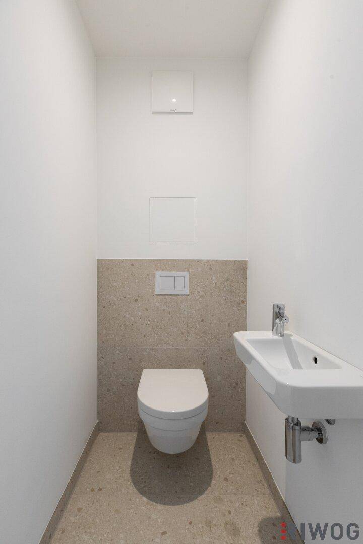 Kleines Gäste-WC mit wandhängender Toilette und kompaktem Waschbecken, modern gefliest.