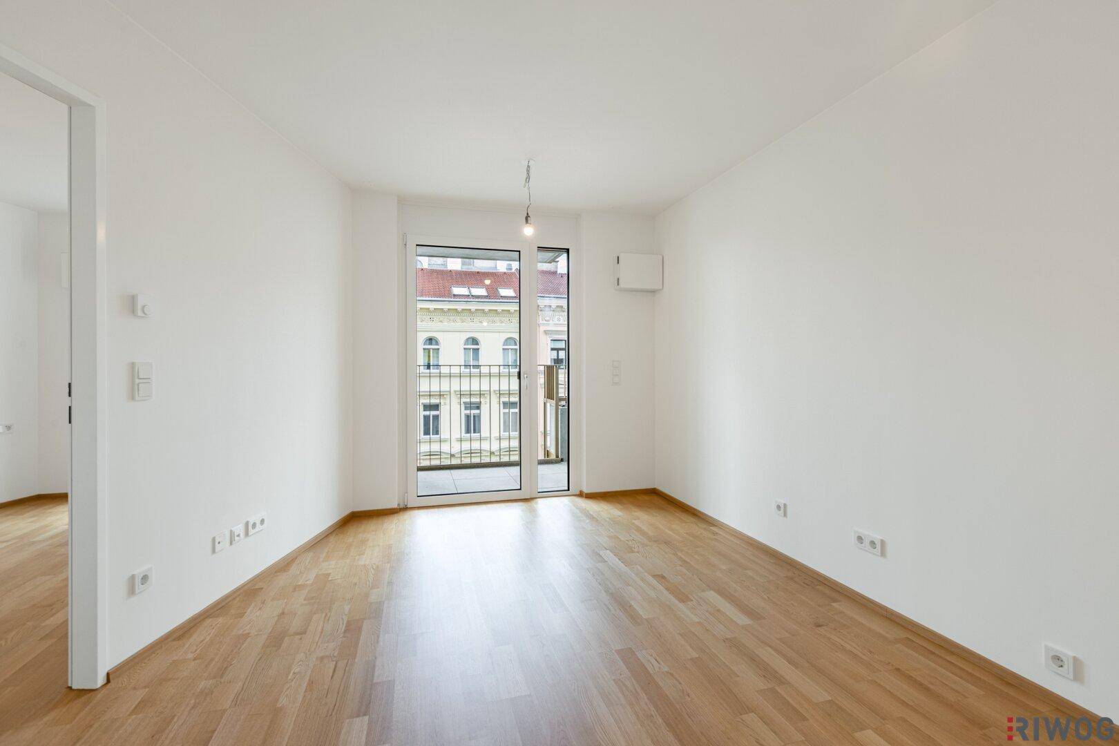 Geräumiges, leeres Wohnzimmer mit Holzboden und direktem Zugang zum Balkon.