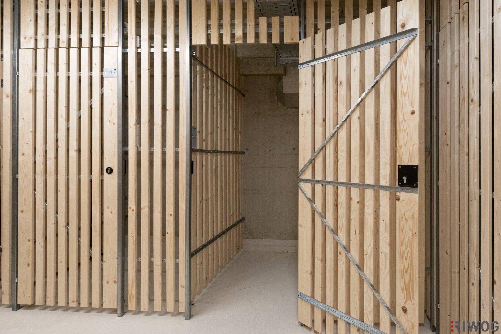 Offene Holztür eines Lagerabteils in einem modernen Kellerraum.