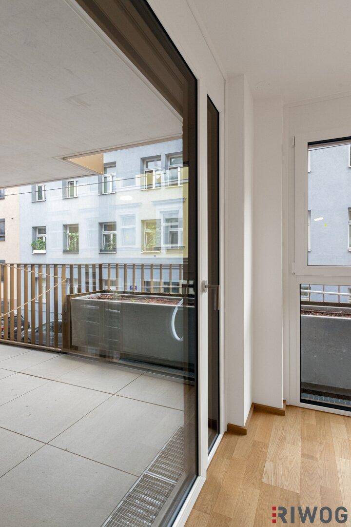 Blick aus einem hellen Zimmer auf den Balkon mit Fliesenboden und umliegenden Gebäuden.