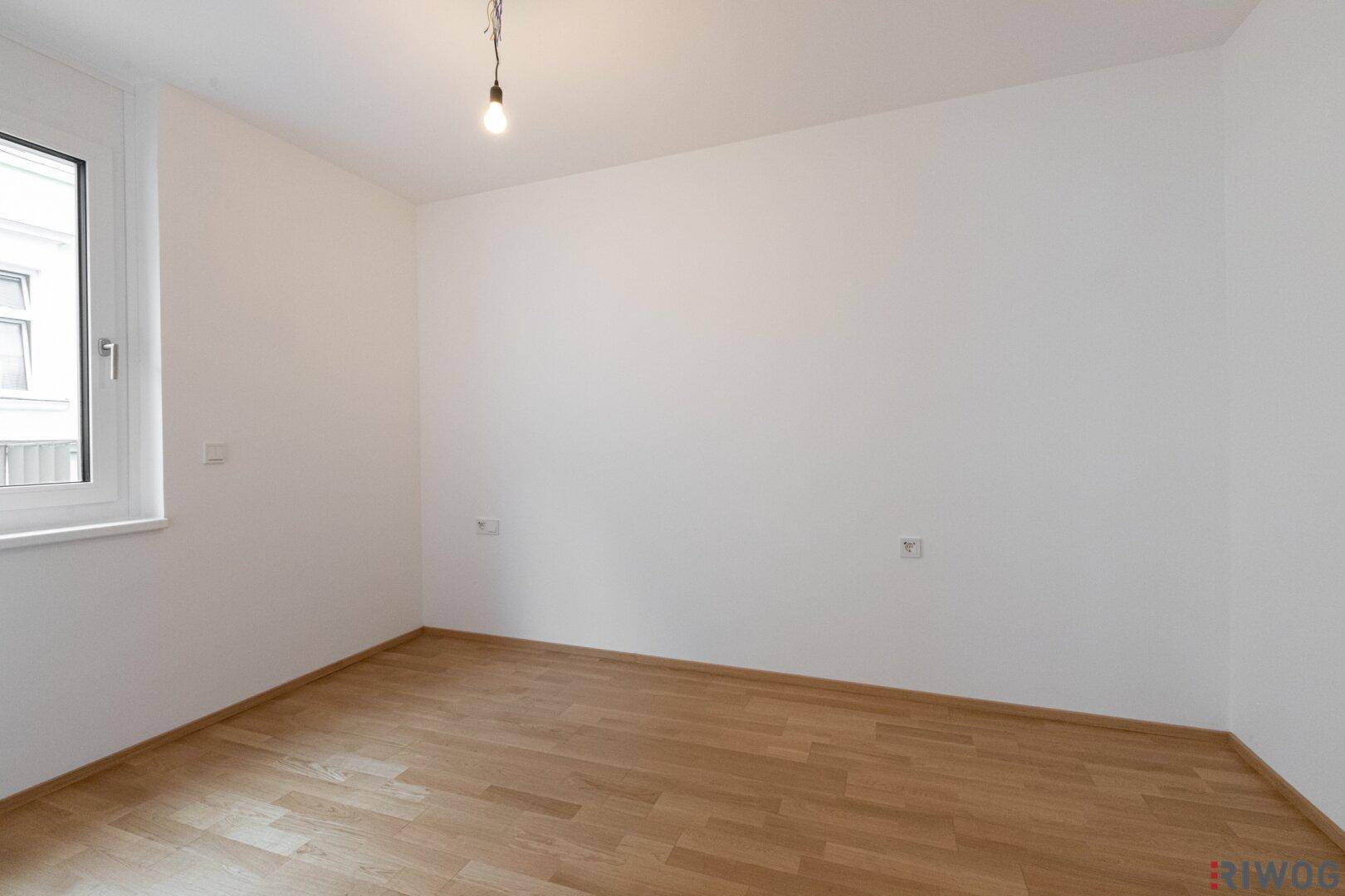 Ruhiges, leeres Zimmer mit Parkettboden und einem Fenster, ideal als Schlaf- oder Arbeitszimmer.