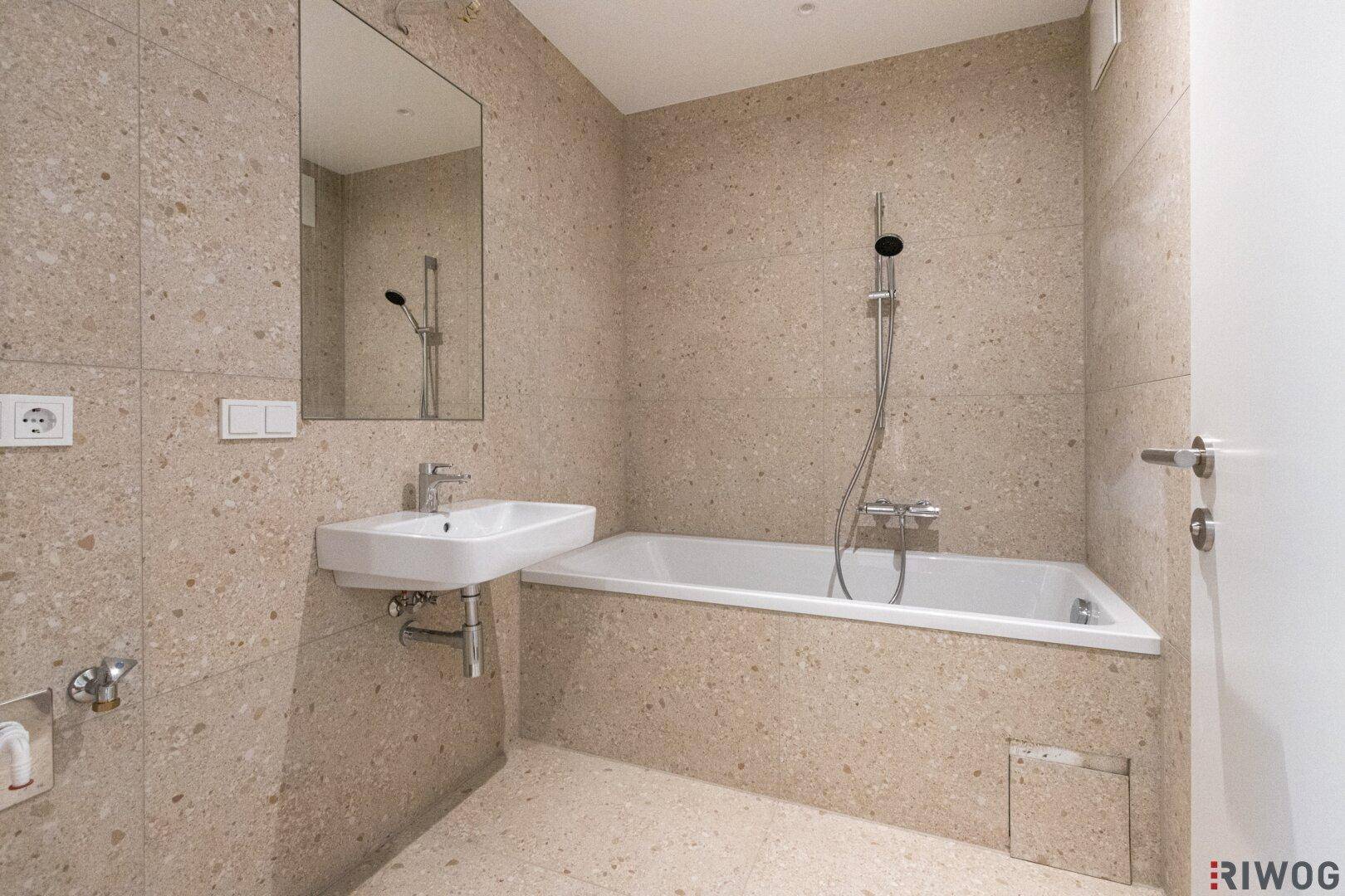 Modernes Badezimmer mit beigefarbenen Fliesen, Badewanne mit Duschfunktion und einem Waschbecken.